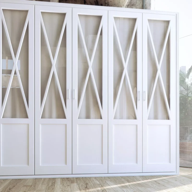 Armario blanco de madera con diseño en X sobre puertas de cristal, en una habitación con suelo de madera y paredes de piedra.